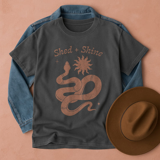 Pepper Comfort Colors tee with snake and sun design, denim jacket, and brown hat on a beige background
