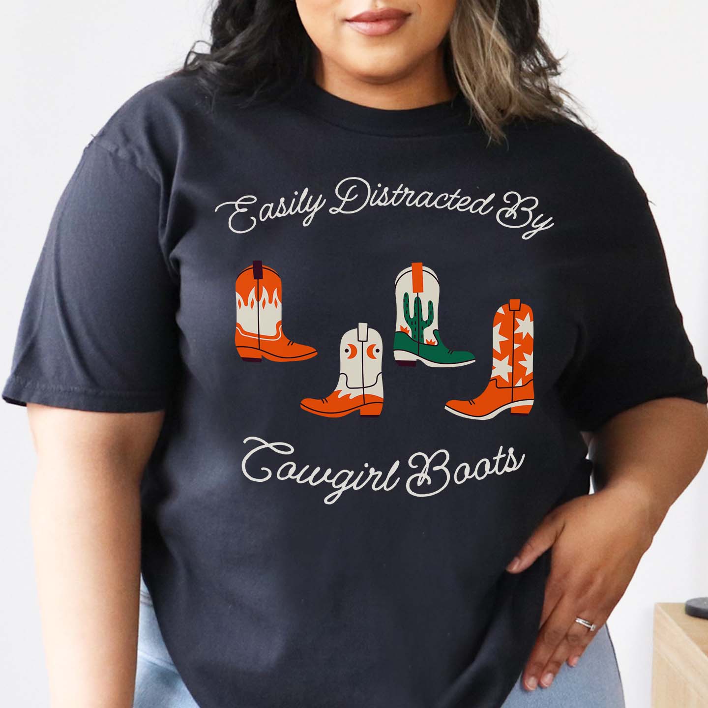 Person wearing a black t-shirt with cowboy boot graphics and text 'Easily Distracted by Cowgirl Boots'.