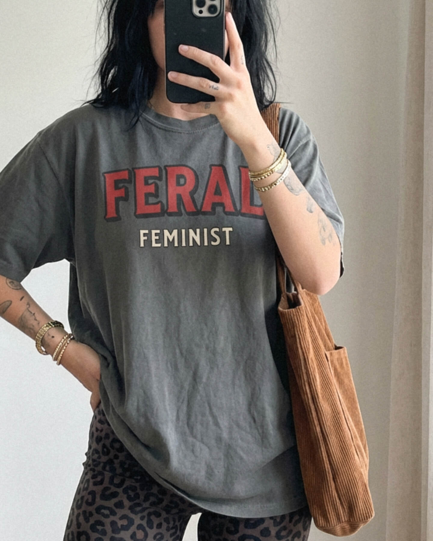 Person wearing a Comfort Colors t-shirt in Pepper color with 'FERAL FEMINIST' text, holding a brown bag.