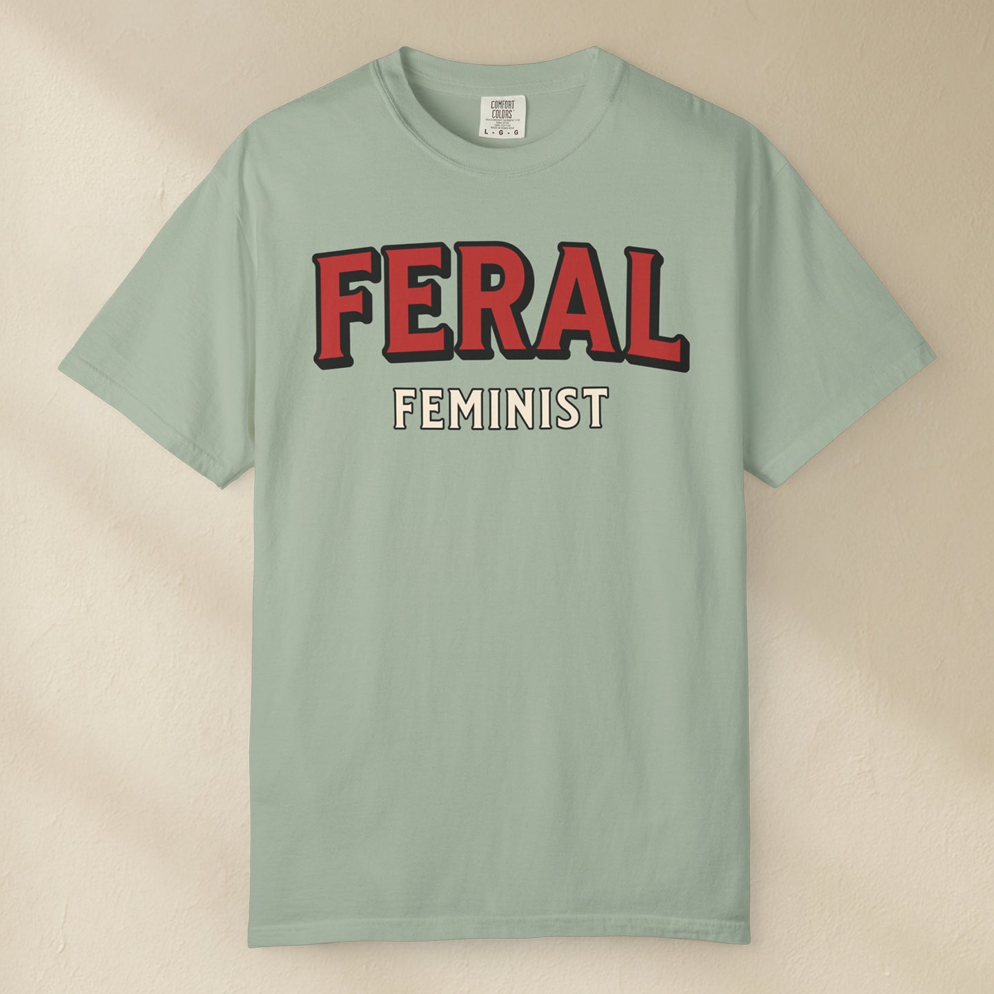Light green t-shirt with 'FERAL FEMINIST' text on a beige background