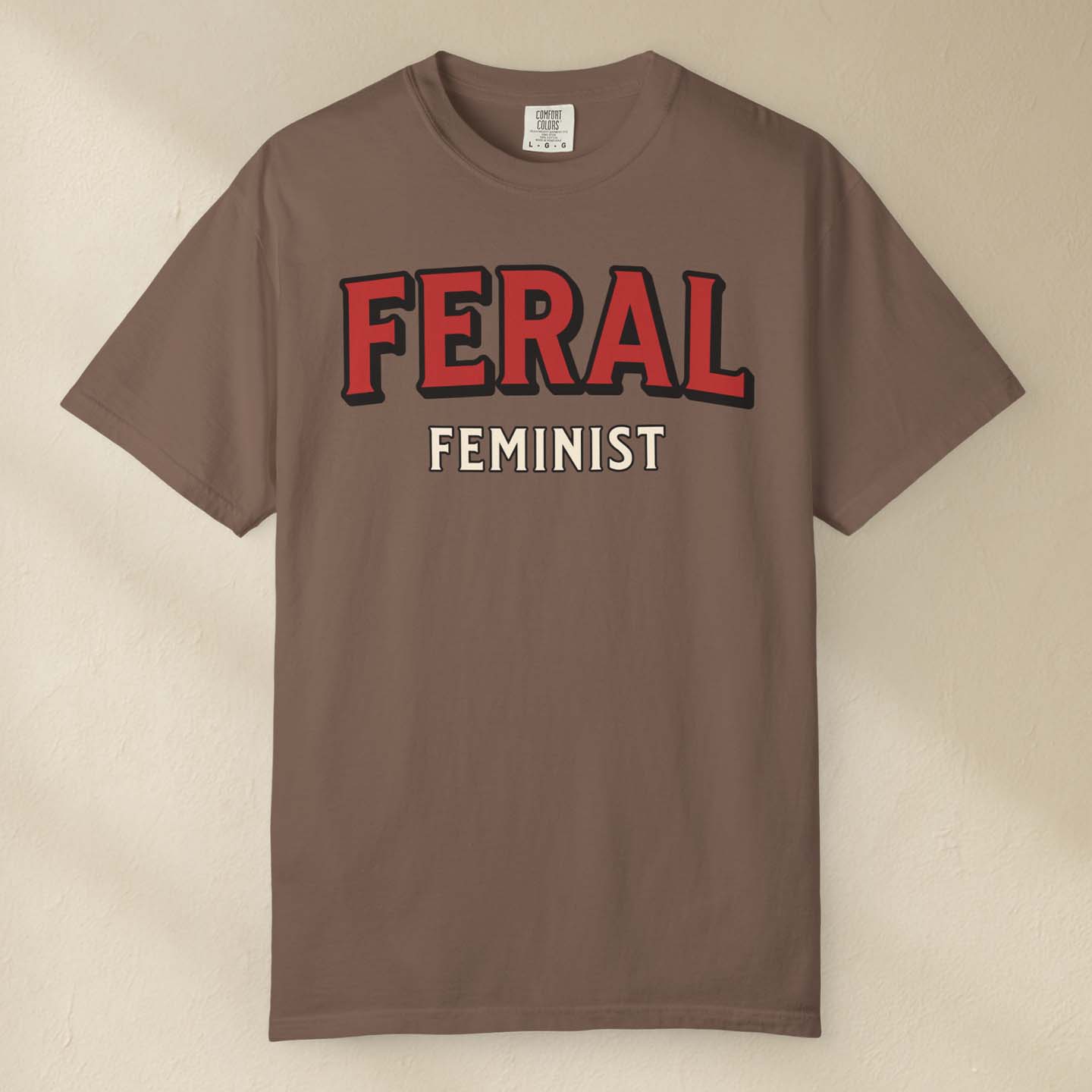 Brown t-shirt with 'FERAL FEMINIST' text on a beige background