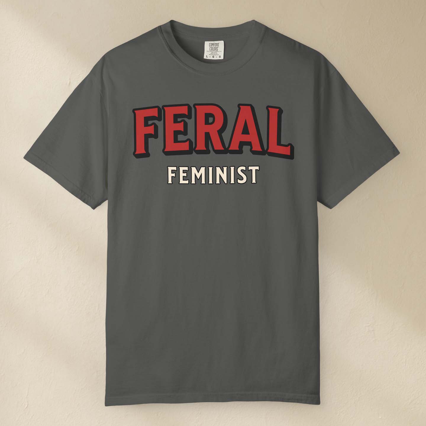 Gray t-shirt with 'FERAL FEMINIST' text in red and white on a beige background