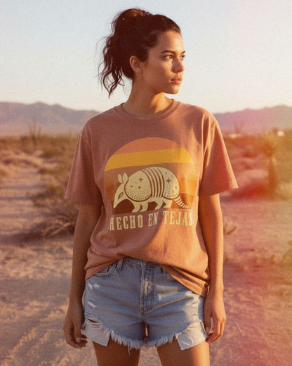 Latina woman wearing a t-shirt with an armadillo graphic and 'Hecho en Tejas' text in a desert setting.