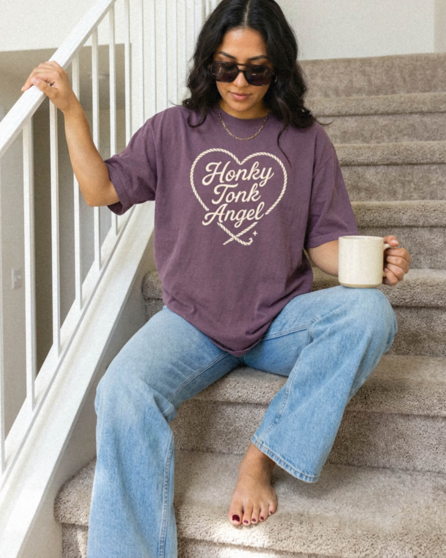 Woman sitting on stairs wearing a Comfort Colors 1717 Berry t-shirt with 'Honky Tonk Angel' text.