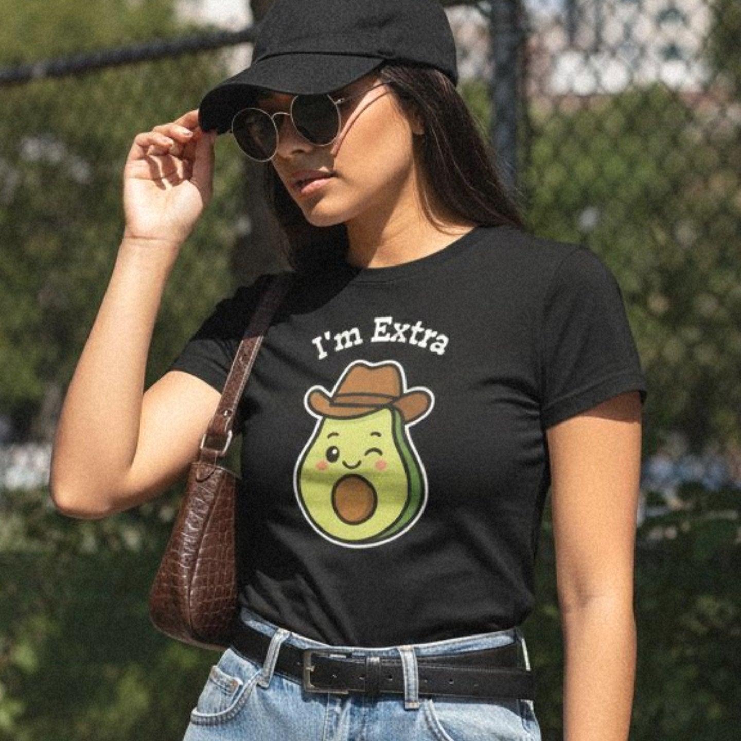 Person wearing a black t-shirt with an avocado cowboy graphic and text 'I'm Extra', outdoors.