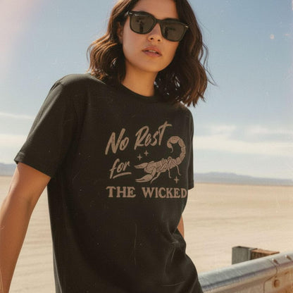 Person wearing a black Comfort Colors 1717 t-shirt with a scorpion graphic and text 'No Rest for the Wicked' in a desert setting
