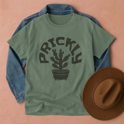 Green t-shirt with cactus graphic and 'PRICKLY' text, blue denim jacket, and brown hat on a peach background