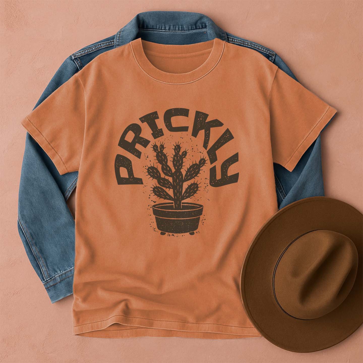 Comfort Colors Yam t-shirt with cactus graphic and 'Prickly' text, blue denim jacket, and brown hat on a beige background