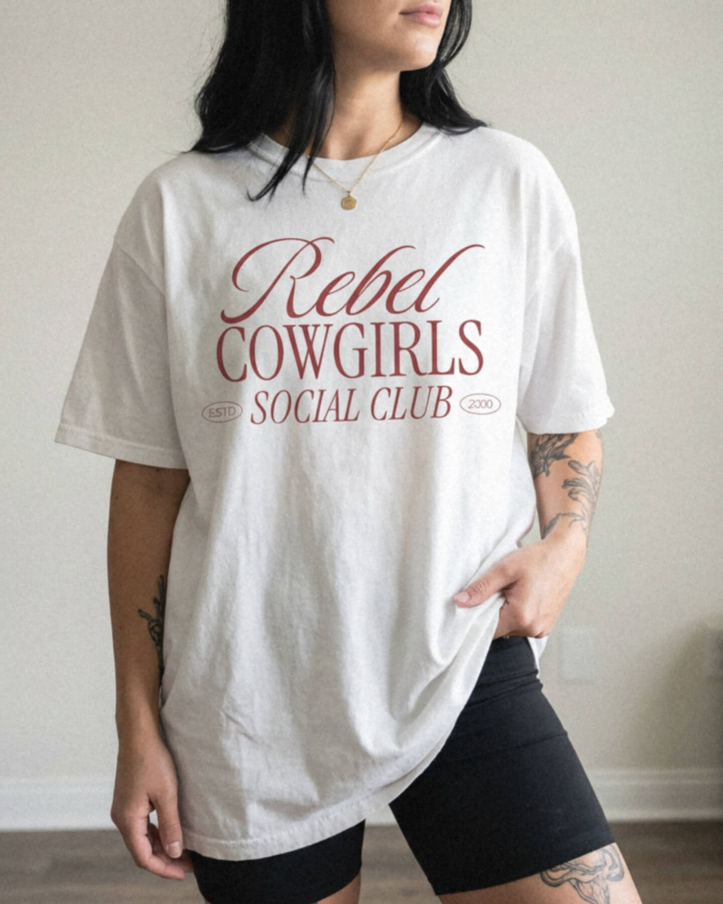 Person wearing a white Comfort Colors t-shirt with 'Rebel Cowgirls Social Club' text.