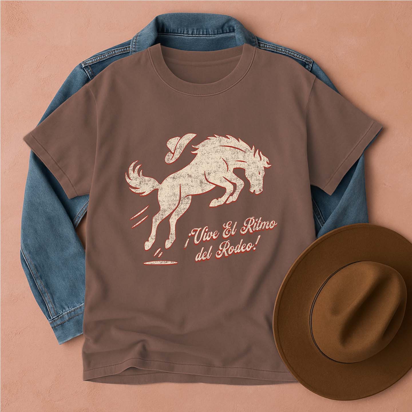 Brown t-shirt with horse graphic and text, blue denim jacket, and brown hat on a beige background